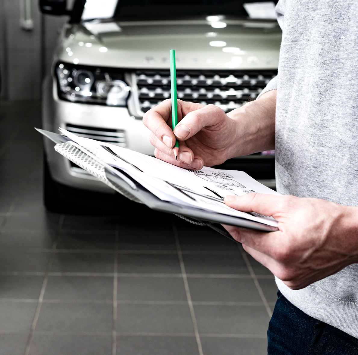 Person holding a clipboard inspecting a vehicle in a showroom
